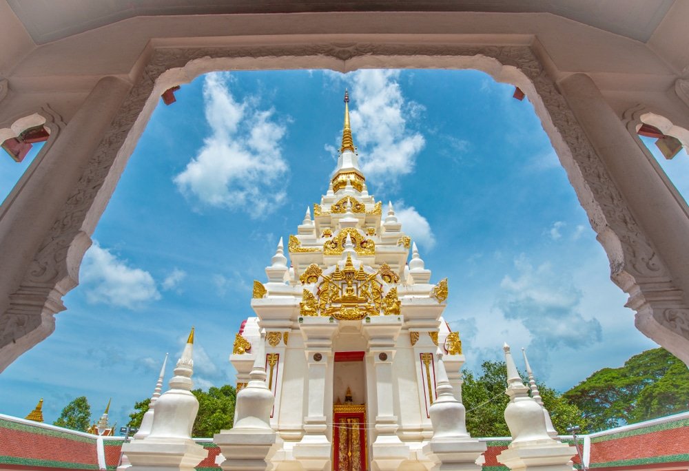 เจดีย์วัดพุทธสีขาวและทองที่ล้อม ที่เที่ยวสุราษฎร์ธานี รอบด้วยโครงสร้างโค้ง ตั้งอยู่ท่ามกลางท้องฟ้าสีครามและเมฆ—หนึ่งในสถานที่ท่องเที่ยวที่น่าตื่นตาตื่นใจของสุราษฎร์ธานีที่นักท่องเที่ยวไม่ควรพลาด.