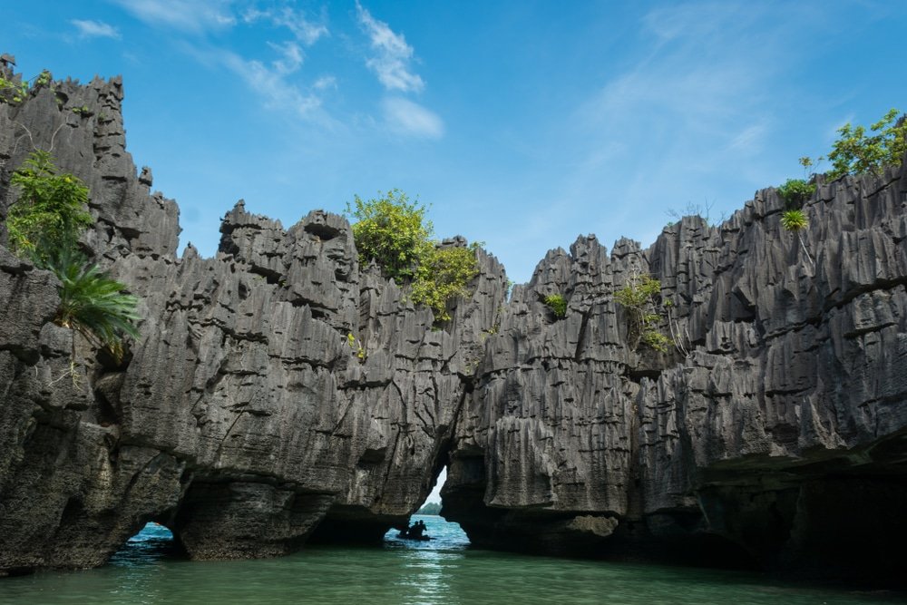 หินปูนรูปร่างขรุขระสูงตระหง่านเหนือผืนน้ำสีเขียวภายใต้ท้องฟ้าสีคราม มีพืชพรรณขึ้นอยู่อย่างกระจัดกระจายบนโขดหิน—เป็นสถานที่ท่องเที่ยวทางธรรมชาติที่เหมาะอย่างยิ่งสำหรับผู้ที่ชื่นชอบการหลีกหนีความวุ่นวายไปสัมผัสความงดงามของธรรมชาติกลางแจ้ง.
