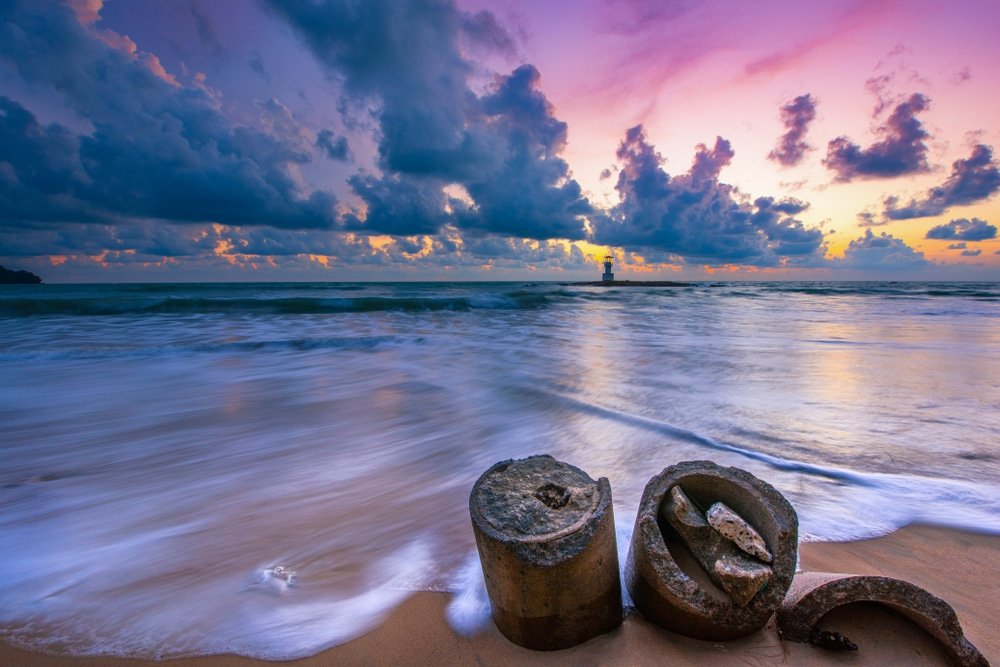 เศษคอนกรีตบนชายหาดทราย คลื่นซัดเข้าฝั่งใต้ท้องฟ้าสีสันสดใสยามพระอาทิตย์ตกดิน—สถานที่ท่องเที่ยวสุดพิเศษในช่วงปลายฝนต้น ที่เที่ยวปลายฝนต้นหนาว หนาว ที่ธรรมชาติและซากอดีตผสานกันอย่างงดงามเงียบสงบ.
