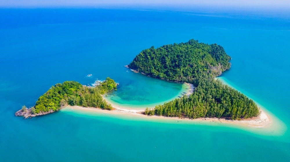 ภาพมุมสูงของเกาะเขียวชอุ่ม—หนึ่งในสถานที่ท่องเที่ยวทางธรรมชาติ—ล้อมรอบด้วยน้ำทะเลสีเทอร์ควอยซ์พร้อมหาดทรายและป่าทึบ.