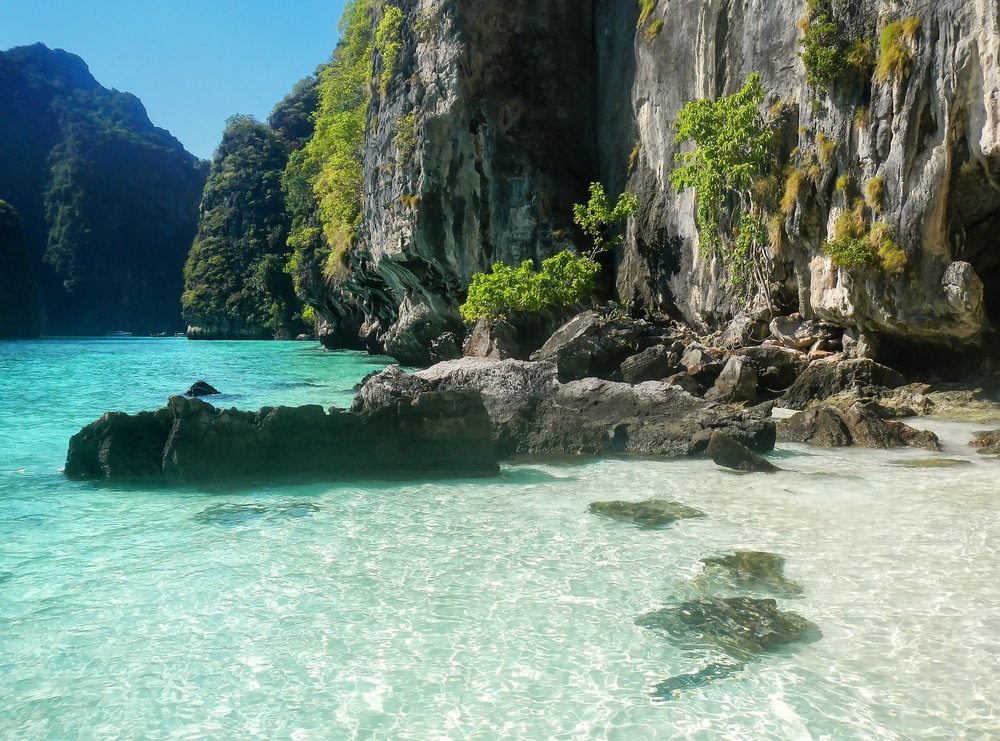 น้ำทะเลสีฟ้าใสและหาดทรายขาวสะอาดพร้อมหน้าผาหินและพืชพรรณสีเขียวภายใต้ท้องฟ้าสีครามสดใส ทำให้สถานที่ท่องเที่ยวทางธรรมชาติแห่งนี้เหมาะอย่างยิ่งสำหรับการพักผ่อนและเพลิดเพลินกับวิวทะเลที่สวยงาม.