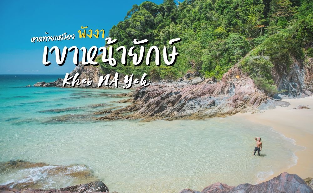 บุคคลหนึ่งยืนอยู่ในน้ำตื้นใกล้ชายฝั่งหินและเนินเขาเขียวชอุ่มที่หาดเขาหนามยักษ์ ซึ่งเป็นสถานที่ท่องเที่ยวธรรมชาติที่ซ่อนตัวอยู่ในจังหวัดพังงา ประเทศไทย.