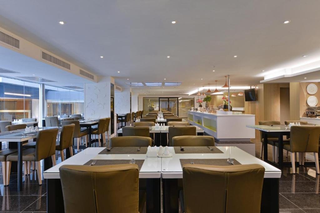 ร้านอาหารสมัยใหม่ที่มีการจัดโต๊ะและเก้าอี้อย่างเป็นระเบียบ, โทนสี ที่เที่ยวกรุงเทพ กลาง, และพื้นที่บุฟเฟ่ต์อยู่ด้านหลังภายใต้แสงไฟอบอุ่น—สถานที่รับประทานอาหารที่น่าดึงดูดใจในกรุงเทพฯ สำหรับคนรักอาหารที่ต้องการผ่อนคลาย.
