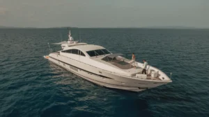 เรือยอชต์หรูสีขาวลอยอยู่บนน้ำสีฟ้าสงบ มีคนสองคนยืนอยู่บนดาดฟ้า.