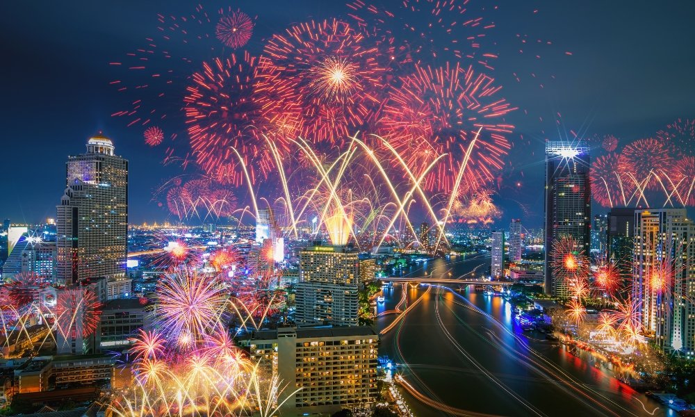 ดอกไม้ไฟสว่างไสวส่องสว่างเส้นขอบฟ้าของกรุงเทพมหานครในยามค่ำคืน  ที่เที่ยวกรุงเทพ สะท้อนเหนือแม่น้ำและตึกระฟ้า สร้างบรรยากาศที่มีชีวิตชีวาในใจกลางเมือง.