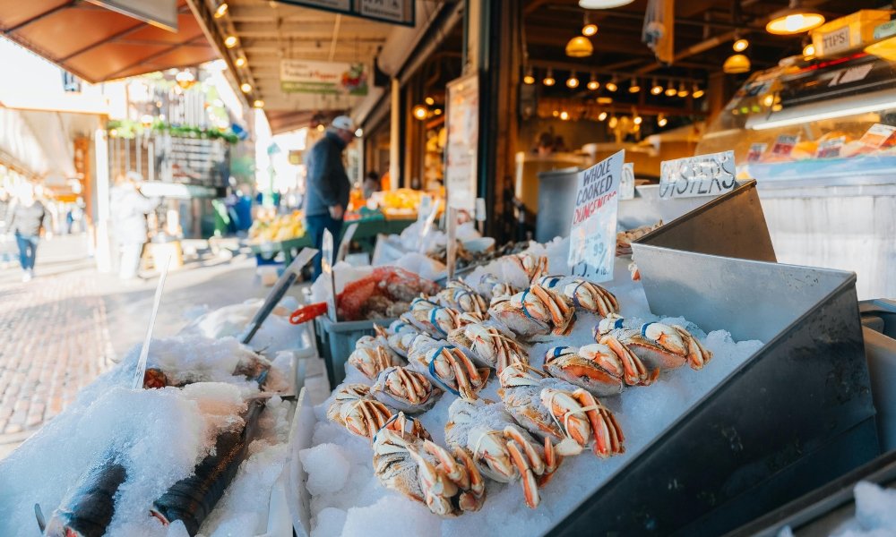 ขาปูสดวางโชว์บนน้ำแข็งในตลาดอาหารทะเลกลางแจ้งในสถานที่ท่องเที่ยวกรุงเทพฯ โดยมีผู้คนและแผงขายของอื่นๆ อยู่เบื้องหลัง. ที่เที่ยวกรุงเทพ 