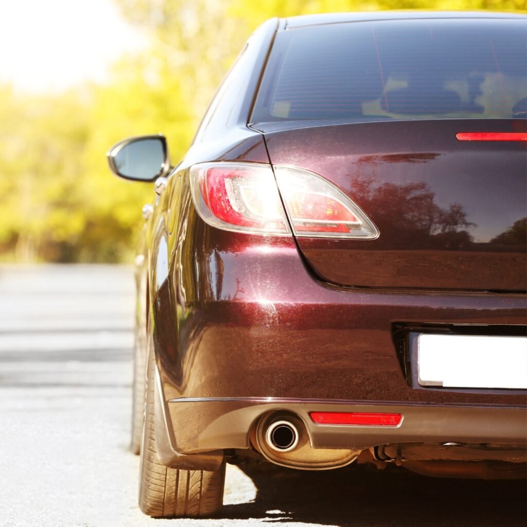 ภาพระยะใกล้ของด้านหลังและด้านซ้ายของรถยนต์สีเข้มที่จอดอยู่บนถนน โดยมีต้นไม้สีเขียวเบลอเป็นฉากหลัง สะท้อนโลโก้ของเว็บปั้มวิวอย่างละเอียดบนพื้นผิวของรถ.