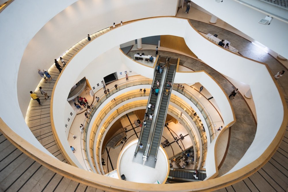 ภาพมุมสูงของภายในอาคารทรงกลมหลายชั้นที่มีบันไดเลื่อนอยู่ตรงกลางและมีผู้คนเดินไปตามทางเดินโค้ง—เป็นอัญมณีทาง ที่เที่ยวกรุงเทพ สถาปัตยกรรมสมัยใหม่และเป็นสถานที่ท่องเที่ยวยอดนิยมในกรุงเทพฯ สำหรับทั้งคนท้องถิ่นและนักท่องเที่ยว.