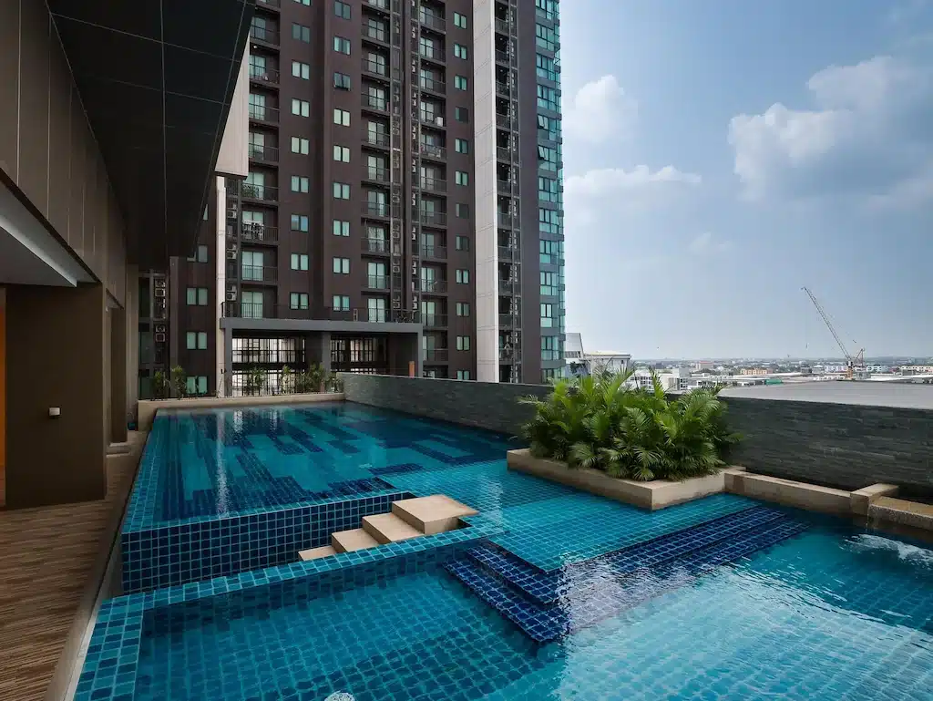 สระว่ายน้ำกลางแจ้งพร้อมกระเบื้องสีน้ำเงิน ตั้งอยู่ติดกับอาคารชุดสูง โรงแรมกรุงเทพ สมัยใหม่ มองเห็นทัศนียภาพของเมืองภายใต้ท้องฟ้าที่มีเมฆบางส่วน—เหมาะสำหรับแขกที่ต้องการการพักผ่อนหรูหราที่ โรงแรม 5 ดาวกรุงเทพ.