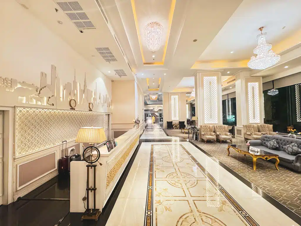 ล็อบบี้ โรงแรม 5 ดาวในกรุงเทพ ฯ ที่สว่างไสวด้วยโคมไฟระย้าอันวิจิตร พื้นหินอ่อนลวดลายสวยงาม เคาน์เตอร์ต้อนรับ และพื้นที่นั่งเล่นพร้อมเก้าอี้และโซฟานุ่มสบาย.