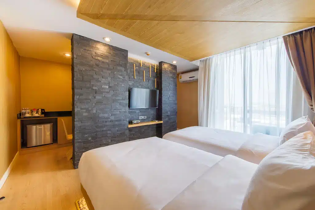 ห้องพักโรงแรมที่ โรงแรม 5 ดาวกรุงเทพ ประกอบด้วยเตียงคู่สองเตียง ผนังตกแต่งด้วยหินพร้อมทีวีติดผนัง มินิบาร์ พื้นที่หน้าต่างบานใหญ่พร้อมผ้าม่านบาง และพื้นไม้หรูหรา.