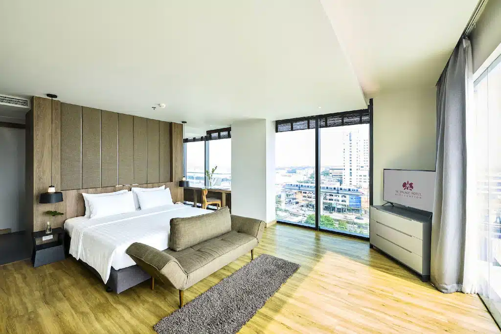 ห้องพักโรงแรมสมัยใหม่พร้อมเตียงขนาดใหญ่, โซฟา, ทีวี, พื้นไม้,  โรงแรมกรุงเทพ หน้าต่างบานใหญ่จากพื้นจรดเพดาน, และวิวเมืองที่สวยงาม—เหมาะสำหรับการเข้าพักของคุณที่โรงแรมในกรุงเทพฯ แห่งนี้.