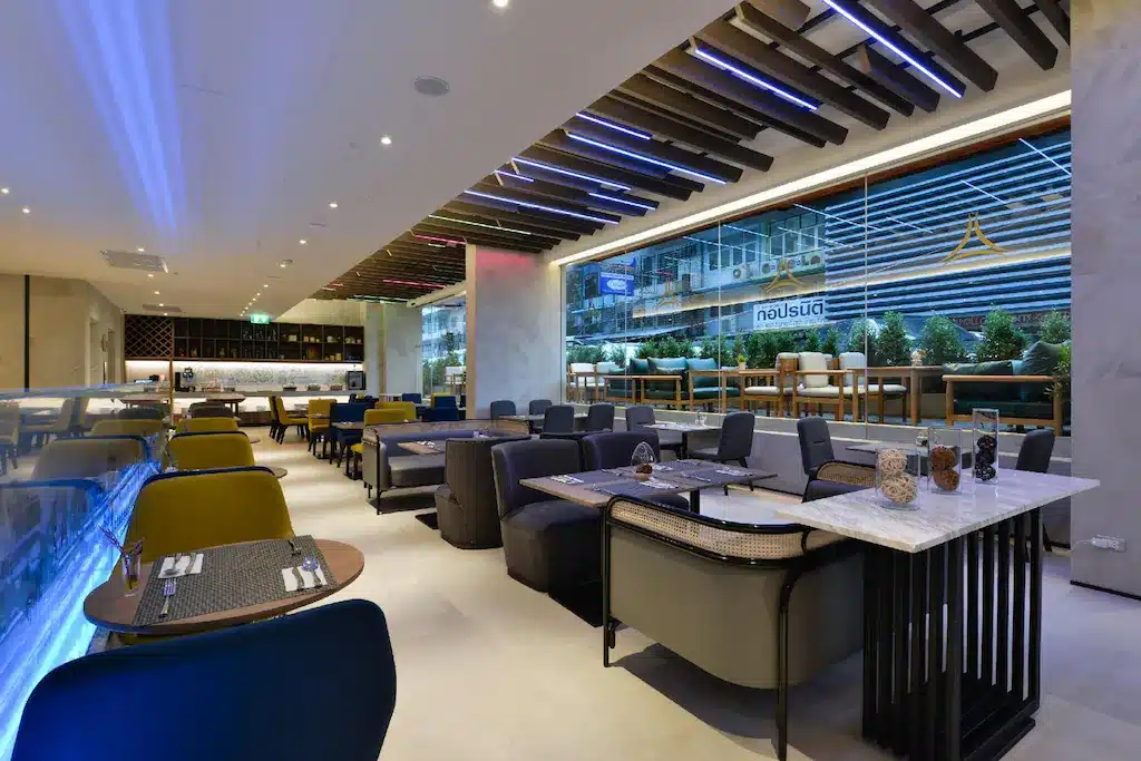 ร้านอาหารสมัยใหม่ที่มีการจัดโต๊ะและเก้าอี้อย่างเป็นระเบียบ พร้อมโคมไฟ โรงแรมกรุงเทพ เพดานตกแต่ง และหน้าต่างบานใหญ่ที่มองเห็นถนนในเมืองในโรงแรม 5 ดาวที่กรุงเทพฯ.
