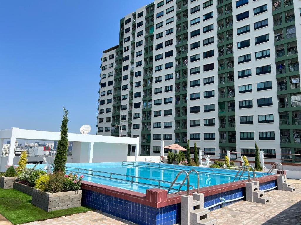 สระว่ายน้ำกลางแจ้งรูปสี่เหลี่ยมผืนผ้าพร้อมบันไดตั้งอยู่บนดาดฟ้าข้างอาคารอพาร์ตเมนต์หลายชั้นในโรงแรมโรในกรุงเทพ ฯ ท่ามกลางท้องฟ้าสีครามสดใส.