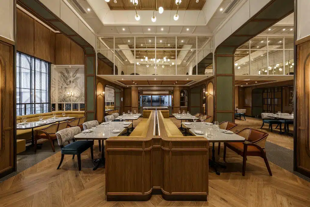 ห้องอาหารกว้างขวางพร้อมพื้นไม้ โคมไฟทันสมัย โต๊ะรับประทานอาหารจัดวางอย่างเป็นระเบียบ ผนัง โรงแรมในกรุงเทพ กระจกเงา และหน้าต่างบานใหญ่ ตั้งอยู่ในโรงแรมระดับ 5 ดาวชื่อดังในกรุงเทพฯ.