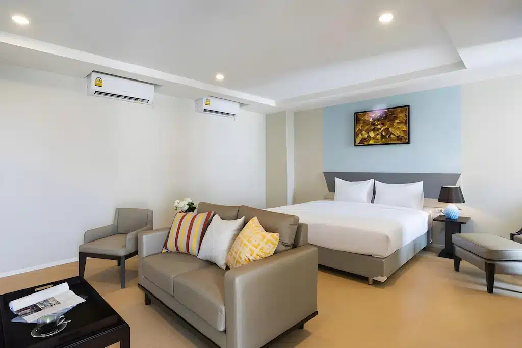 ห้องพักโรงแรมสมัยใหม่ที่ โรงแรม 5 ดาวกรุงเทพ, ประกอบด้วยเตียงคู่,  โรงแรมกรุงเทพ โซฟาขนาดเล็ก, เก้าอี้, โต๊ะกาแฟ, โคมไฟข้างเตียง, ภาพศิลปะผนังสไตล์, และเครื่องปรับอากาศสองตัวบนผนังสีขาว.