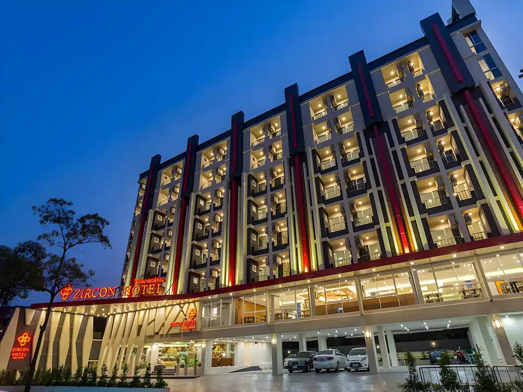 อาคารโรงแรมหลายชั้นที่ทันสมัยพร้อมระเบียงและภายนอกที่ส่อง โรงแรมกรุงเทพ สว่างในยามพลบค่ำ รถยนต์จอดอยู่ด้านหน้า และป้ายที่เขียนว่า "โรงแรมเซอร์คอน"—ทางเลือกที่น่าดึงดูดสำหรับผู้ที่มองหา โรงแรมกรุงเทพ สำหรับการเข้าพัก.