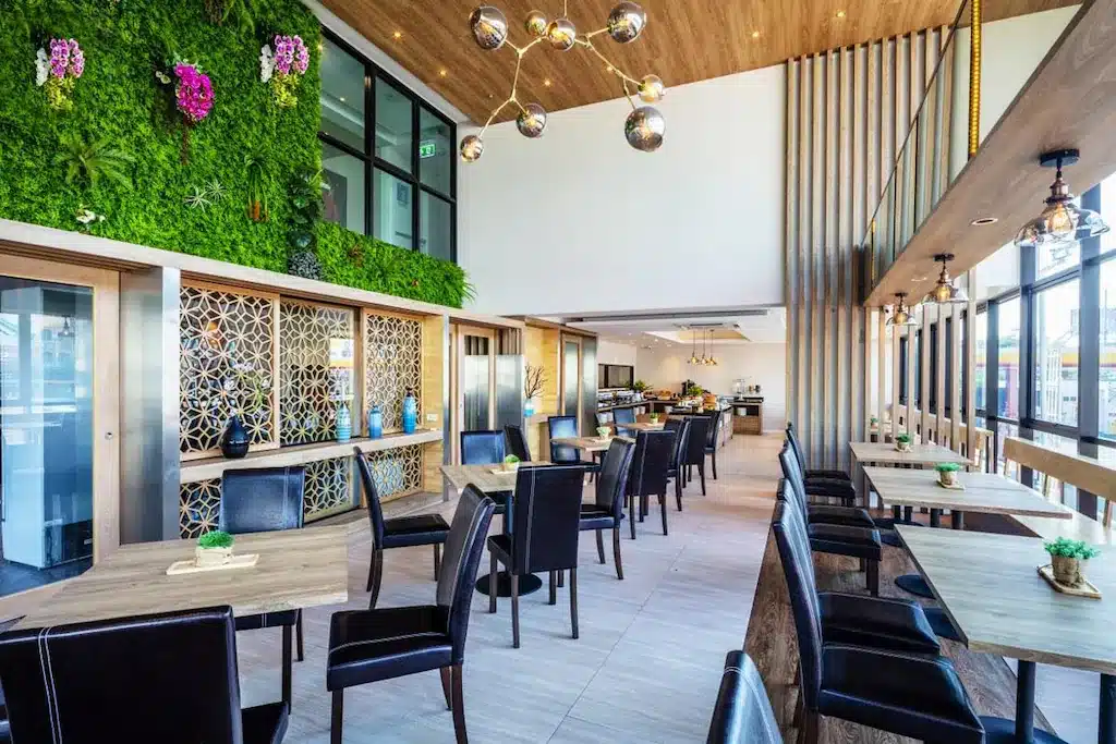 พื้นที่รับประทานอาหารสมัยใหม่ที่ โรงแรม 5 ดาวกรุงเทพ พร้อมโต๊ะไม้ เก้าอี้สีดำ หน้าต่างบานใหญ่ ผนังตกแต่งด้วยพืชสีเขียว และโคมไฟสไตล์ร่วมสมัย.
