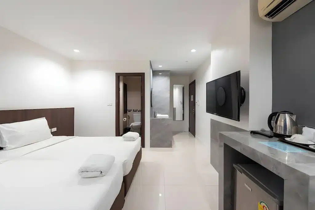 ห้องพักโรงแรมสมัยใหม่พร้อมเตียงคู่, ทีวีติดผนัง, ตู้เย็นขนาดเล็ก, ชุดกาต้มน้ำไฟฟ้า, และห้องน้ำในตัวที่ โรงแรมในกรุงเทพ สามารถมองเห็นได้ผ่านประตูเปิด—เหมาะสำหรับการเข้าพักของคุณที่ โรงแรมกรุงเทพ.