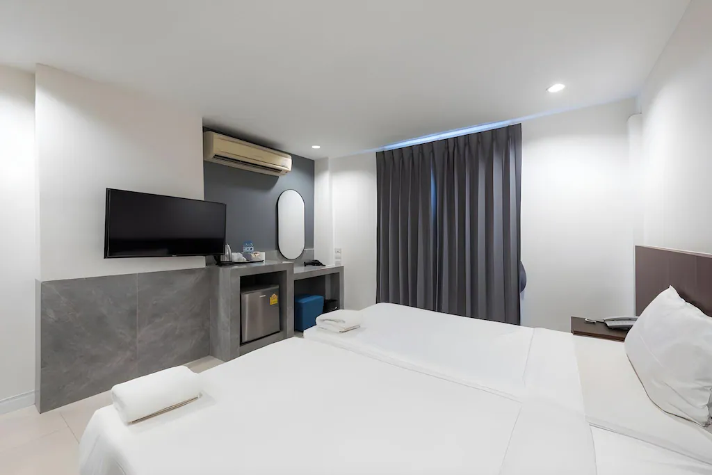 ห้องพักโรงแรม 5 ดาวกรุงเทพที่ทันสมัย พร้อมเตียงเดี่ยวสองเตียง  โรงแรมในกรุงเทพ โทรทัศน์ติดผนัง ตู้เย็นขนาดเล็ก โต๊ะพร้อมกระจก และม่านทึบแสงปิดสนิท—เหมาะสำหรับผู้ที่มองหาที่พักกรุงเทพที่มีสไตล์.