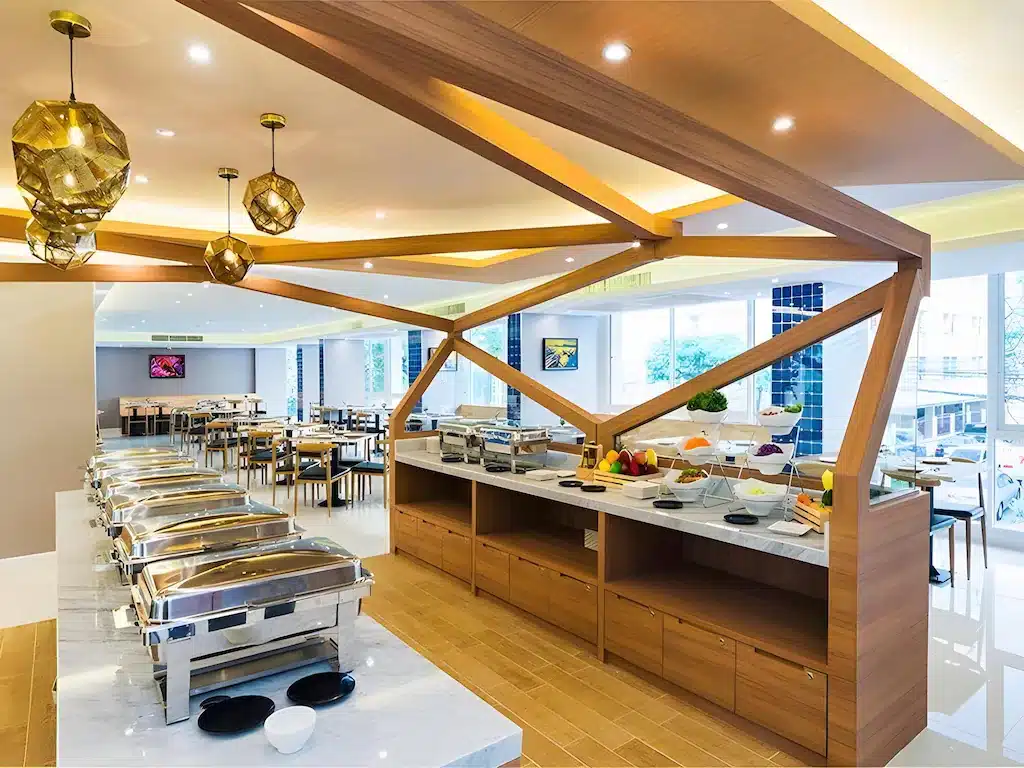 ร้านอาหารบุฟเฟ่ต์สมัยใหม่พร้อมถาดอุ่นอาหาร, การจัดแสดงอาหาร, และโต๊ะเก้าอี้ที่จัดเรียงอย่างเป็นระเบียบในพื้นที่รับประทานอาหารที่สว่างและกว้างขวาง ณ โรงแรม 5 ดาวในกรุงเทพฯ.