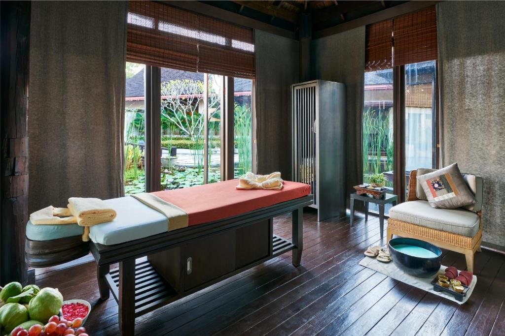 ห้องทรีตเมนต์สปาพร้อมเตียงนวด ผ้าขนหนู เก้าอี้ อ่างแช่เท้า และวิวสวนบ่อน้ำที่เงียบสงบผ่านหน้าต่างบานใหญ่—เหมาะอย่างยิ่งสำหรับการผ่อนคลายหลังจากสำรวจสถานที่ท่องเที่ยวเขาใหญ่.