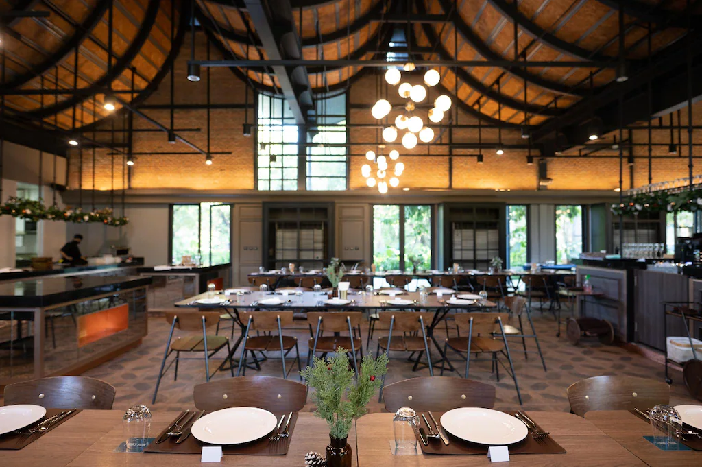 ร้านอาหารภายในที่กว้างขวางและทันสมัย พร้อมโต๊ะไม้สำหรับรับประทานอาหาร เก้าอี้จัดเรียงอย่างเป็นระเบียบ และหน้าต่างบานใหญ่—สถานที่เชิญชวนให้คุณได้ผ่อนคลายหลังจากสำรวจ ที่เที่ยวเขาใหญ่ หรือเยี่ยมชม สถานที่ท่องเที่ยวเขาใหญ่.