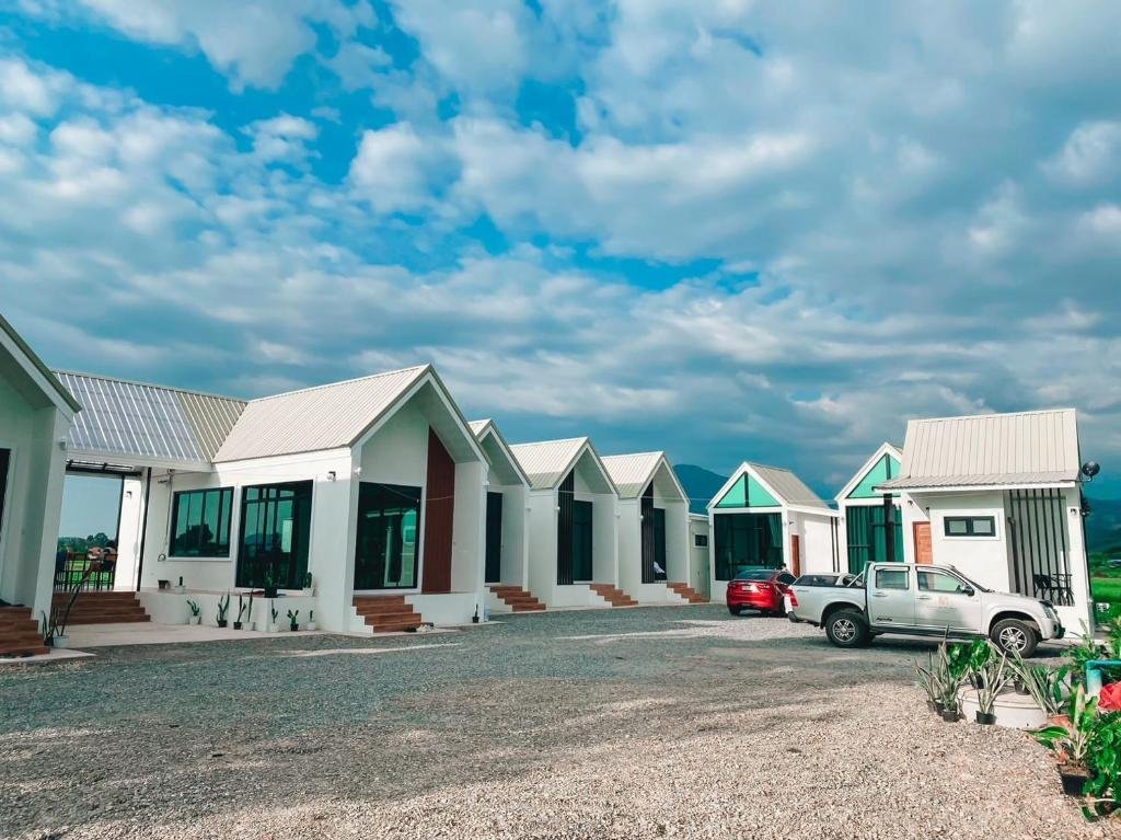 แถวของบ้านพักตากอากาศสีขาวสมัยใหม่ที่มีหน้าต่างบานใหญ่และหลังคาทรงจั่ว รถยนต์สองคันจอดอยู่ด้านหน้า ภายใต้ท้องฟ้าที่มีเมฆบางส่วน—เหมาะอย่างยิ่งสำหรับการพักผ่อนและท่องเที่ยวในน่านในบรรยากาศที่เงียบสงบ.