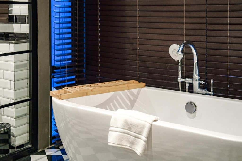 ห้องน้ำสไตล์โมเดิร์นพร้อมอ่างอาบน้ำแบบลอยตัวสีขาว ถาดอาบน้ำไม้ ก๊อกน้ำโครเมียม และม่านบังตาแนวนอนสีเข้มในพื้นหลัง—เหมาะสำหรับการผ่อนคลายหลังจากสำรวจสถานที่ท่องเที่ยวเขาใหญ่.