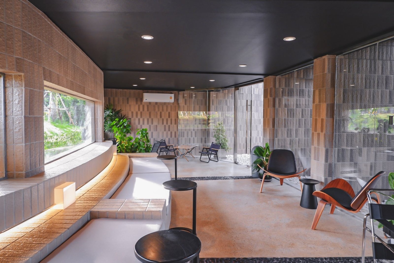 พื้นที่นั่งเล่นสมัยใหม่พร้อมผนังบล็อกคอนกรีต เฟอร์นิเจอร์สไตล์มินิมอล ต้นไม้ ม้านั่งบิวท์อินพร้อมไฟส่องสว่าง และหน้าต่างบานใหญ่ที่มองเห็นวิวสีเขียว—แรงบันดาลใจที่สมบูรณ์แบบสำหรับผู้ที่กำลังมองหา ที่เที่ยวเขาใหญ่ ที่ทั้งมีสไตล์และสะดวกสบาย.