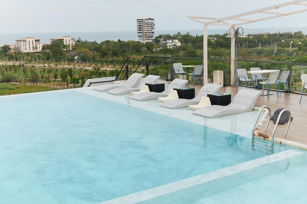 สระว่ายน้ำอินฟินิตี้บนดาดฟ้าพร้อมเก้าอี้อาบแดดแบบจมน้ำ ที่นั่งบนดาดฟ้า และวิวทะเลในบรรยากาศที่มีเมฆครึ้ม ณ โรงแรมหัวหินสุดเก๋ สำหรับการพักผ่อนริมทะเลที่สมบูรณ์แบบของคุณ.