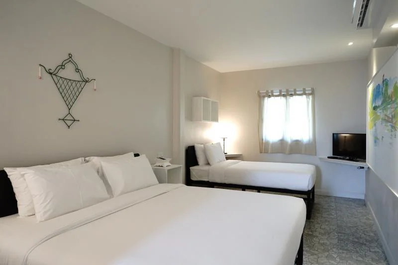 ห้องพักโรงแรมที่ โรงแรมอยุธยา พร้อมเตียงคู่สองเตียง ผ้าปูที่นอนสีขาว โทรทัศน์ติดผนัง หน้าต่างพร้อมผ้าม่าน และการตกแต่งน้อยนิดบนผนังสีอ่อน.