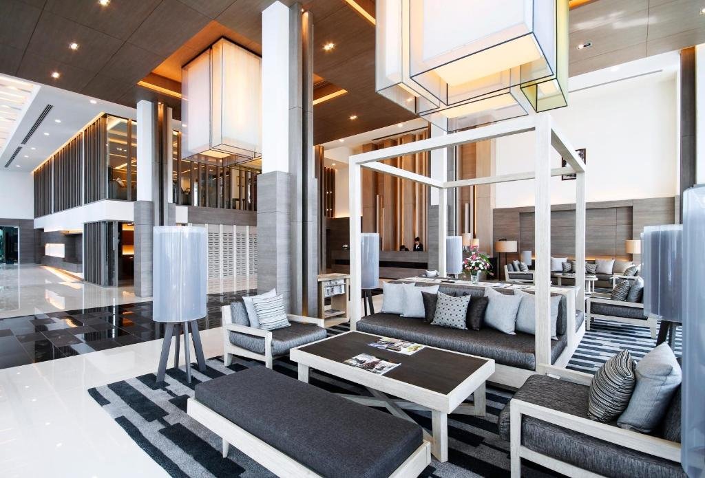 ล็อบบี้โรงแรมสมัยใหม่พร้อมเฟอร์นิเจอร์สีเทาและขาว โคมไฟรูปทรงเรขาคณิต พรมลายทาง และหน้าต่างบานใหญ่ที่สร้างบรรยากาศสว่างและเปิดโล่ง—เหมาะสำหรับการพักผ่อนหลังจากวันแห่งการสำรวจสถานที่ท่องเที่ยวในอยุธยา.