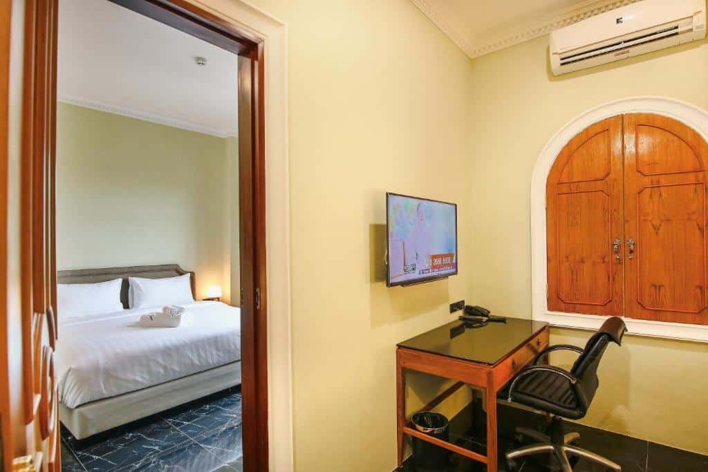 ห้องนอนที่อบอุ่นพร้อมเตียงคู่สามารถมองเห็นได้ผ่านประตูที่เปิดอยู่; ในด้านหน้า ที่พักหัวหินราคาถูก มีโต๊ะทำงาน เก้าอี้ โทรทัศน์ติดผนัง โทรศัพท์ และหน้าต่างพร้อมบานประตูไม้สำหรับพักผ่อนอย่างสบาย.