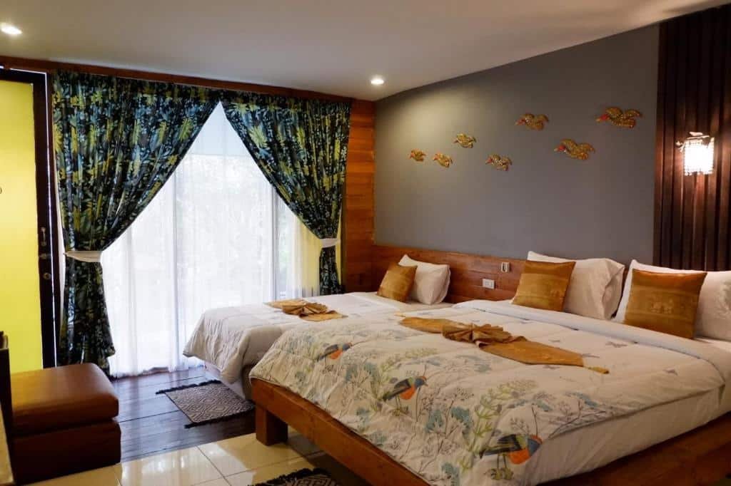 ห้องพักโรงแรมที่ โรงแรมอยุธยา พร้อมเตียงสองเตียง ผ้าปูที่นอนลายสวย หมอนสีเหลือง ผ้าม่านสไตล์ทรอปิคอล ไม้ตกแต่ง และของตกแต่งรูปปลาบนผนังสีเทา.