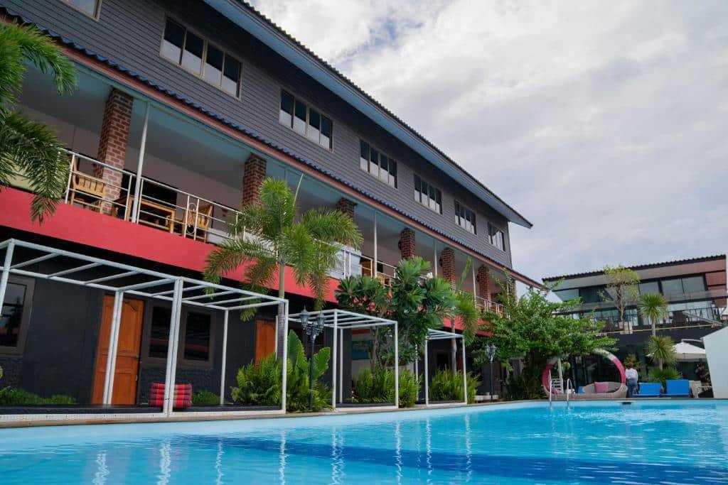 ที่พักอยุธยาสมัยใหม่สามชั้นพร้อมระเบียงมองเห็นสระว่ายน้ำกลางแจ้งขนาดใหญ่ ล้อมรอบด้วยต้นปาล์มและพืชพรรณเขียวขจีภายใต้ท้องฟ้าที่มีเมฆปกคลุม.