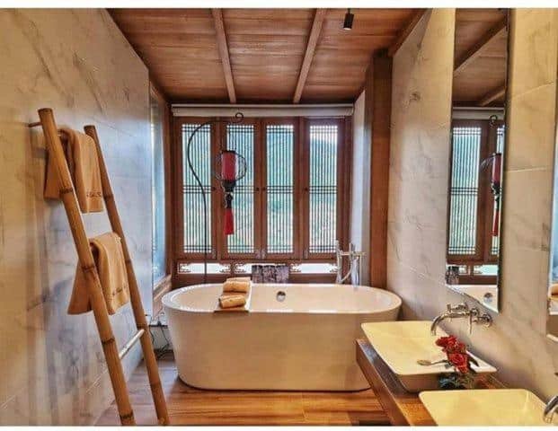 ห้องน้ำสไตล์โมเดิร์นพร้อมอ่างอาบน้ำแบบลอยตัวใกล้หน้าต่างบานใหญ่ เพดานไม้ อ่างล้างหน้าคู่ และราวแขวนผ้าขนหนู—เหมาะสำหรับการผ่อนคลายหลังจากเที่ยวชมสถานที่ท่องเที่ยวในอยุธยาหรือใช้เวลาทั้งวันที่แหล่งท่องเที่ยวในอยุธยา.