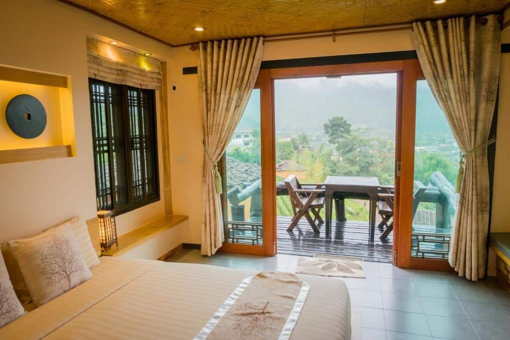 เตียงที่จัดไว้อย่างเรียบร้อยในห้องที่อบอุ่น พร้อมประตูบานกระจกขนาดใหญ่เปิดออกสู่ระเบียงเล็ก ๆ ที่มีโต๊ะและเก้าอี้สองตัว มองเห็นทิวทัศน์ภูเขาสีเขียวขจี—เหมาะอย่างยิ่งสำหรับการพักผ่อนหลังจากเที่ยวชมสถานที่ท่องเที่ยวในอยุธยา.