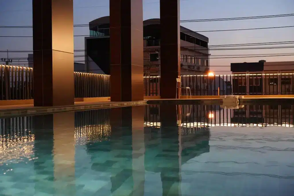 สระว่ายน้ำกลางแจ้งที่มีน้ำสงบล้อมรอบด้วยเสาสูงและอาคารในพื้นหลังยามพลบค่ำ มอบบรรยากาศเงียบสงบที่เป็นเอกลักษณ์ของ โรงแรมหัวหิน สำหรับการพักผ่อนที่ผ่อนคลาย.
