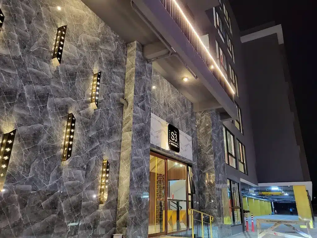 ภาพยามค่ำคืนของทางเข้าอาคารสมัยใหม่ที่มีผนังลายหินอ่อน ไฟแนวตั้ง ประตูกระจก และป้ายไฟ "S3 Residen" ที่สว่างไสว—ตัวเลือกที่น่าดึงดูดสำหรับ ที่พักหัวหินราคาถูก หรือผู้ที่มองหา โรงแรมหัวหิน ที่มีสไตล์.