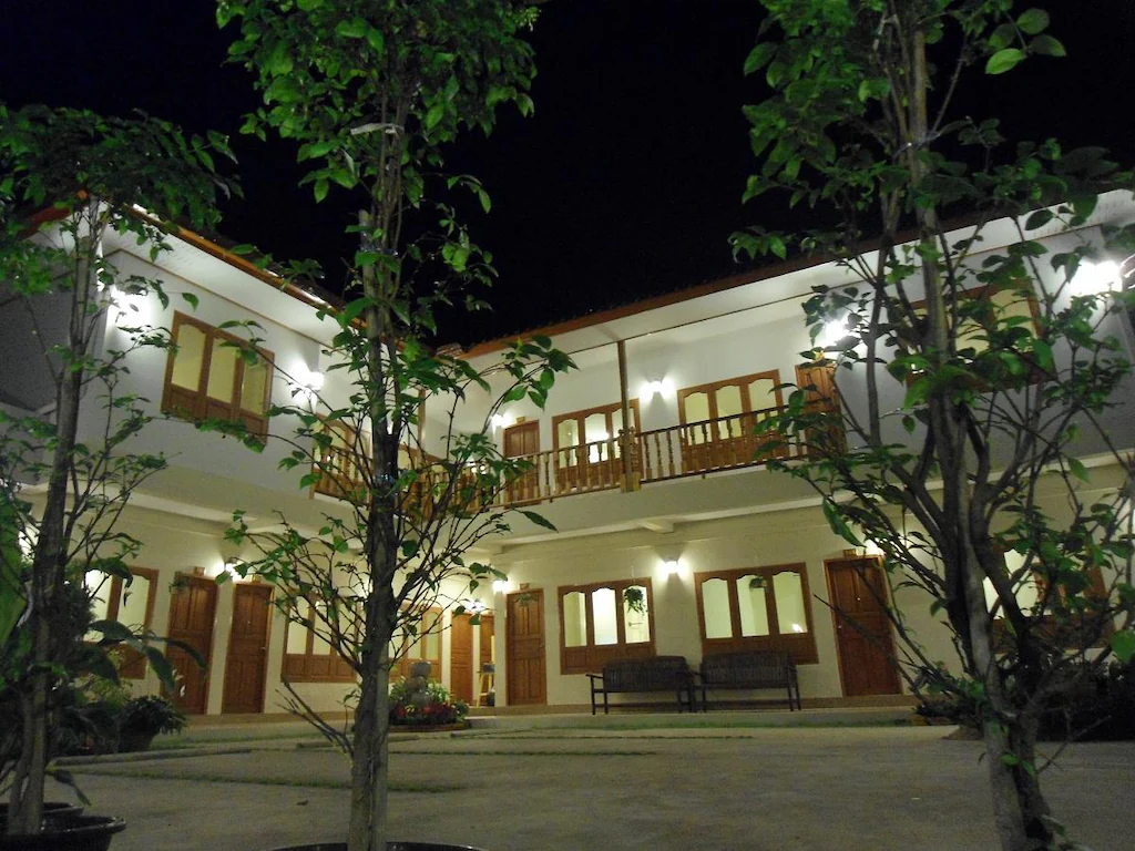 อาคารสองชั้นที่มีประตูและหน้าต่างไม้ถูกส่องสว่างด้วยไฟภายนอกในยามค่ำคืน; ต้นไม้สองต้นที่มีใบหนาแน่นยืนอยู่ในเบื้องหน้า มอบที่พักอบอุ่นให้กับนักเดินทางที่แสวงหาความสะดวกสบายใกล้ที่พักในเมืองน่าน.