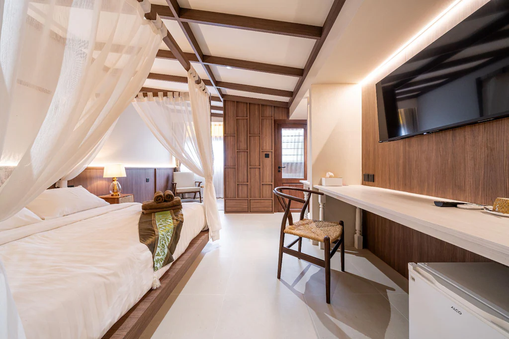 ห้องพักโรงแรมที่ โรงแรมอยุธยา พร้อมเตียงผ้าใบ, โต๊ะทำงาน, เก้าอี้, โทรทัศน์จอแบน, ตู้เย็นขนาดเล็ก, ไม้ตกแต่ง, และแสงสว่างนุ่มนวล ผ้าเช็ดตัววางไว้บนเตียงเพื่อความสะดวกสบายของคุณ.