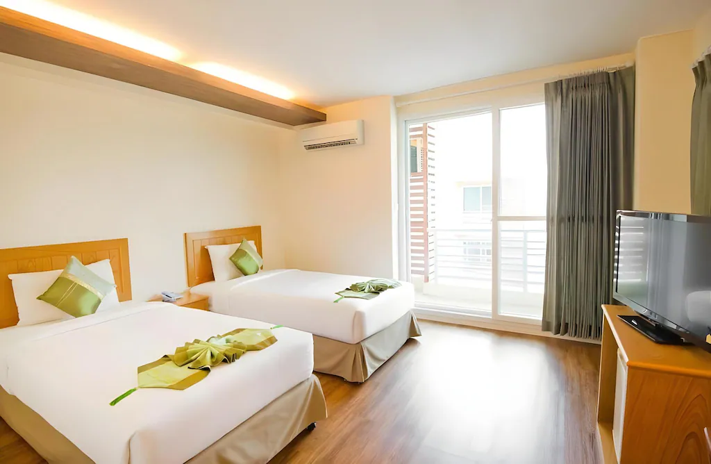 สัมผัสความสะดวกสบายที่ โรงแรมอยุธยา แห่งนี้ พร้อมเตียงเดี่ยวสองเตียง หมอนตกแต่งสีเขียว ผ้าตกแต่ง ผ้าปูที่นอน โทรทัศน์จอแบน พื้นไม้ และหน้าต่างบานใหญ่พร้อมผ้าม่าน.