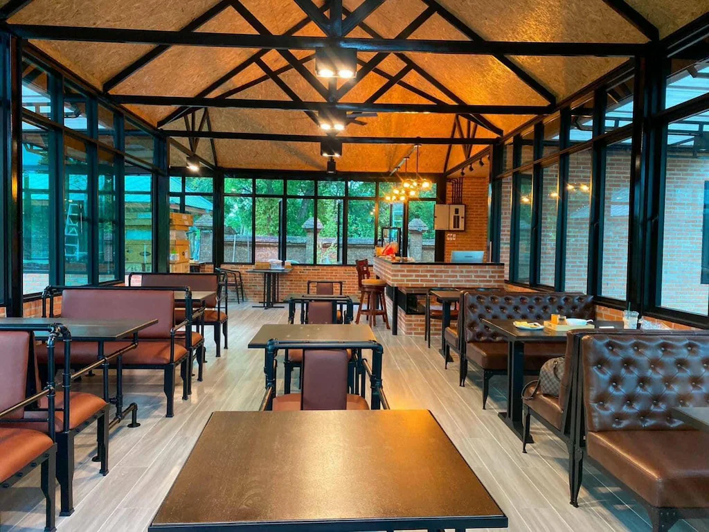 การตกแต่งภายในคาเฟ่สมัยใหม่ที่โรงแรมอยุธยา พร้อมที่นั่งหนังสีน้ำตาล โต๊ะสีดำ หน้าต่างบานใหญ่ และคานไม้เปลือย โดดเด่นด้วยผนังอิฐและแสงธรรมชาติที่ส่องผ่านผนังกระจก.