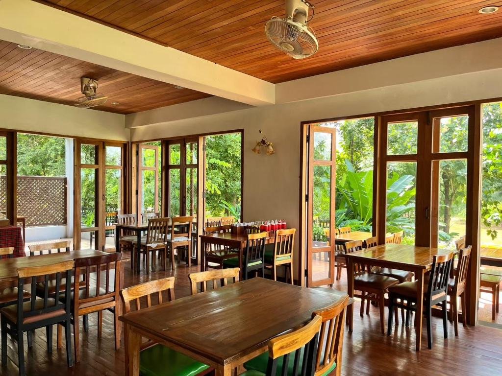 พื้นที่รับประทานอาหารในร้านอาหารที่สว่างไสวและว่างเปล่า มีโต๊ะและเก้าอี้ไม้ หน้าต่างบานใหญ่ และประตูที่เปิดออกสู่สวนสีเขียวด้านนอก—จุดแวะพักที่น่าดึงดูดสำหรับผู้ที่กำลังสำรวจสถานที่ท่องเที่ยวในอยุธยา.