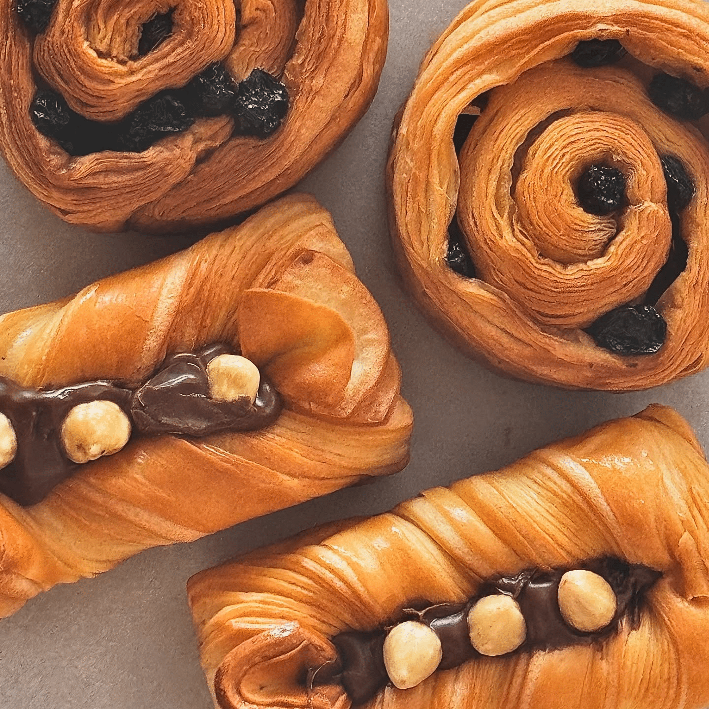 ขนมอบสี่ชิ้นวางอยู่บนพื้นผิวสีอ่อน สองชิ้นมีชั้นวนและลูกเกด และอีกสองชิ้นไส้ครีมช็อกโกแลตและโรยด้วยเฮเซลนัท—ของว่างที่เหมาะอย่างยิ่งหลังจากสำรวจสถานที่ท่องเที่ยวเชียงใหม่.