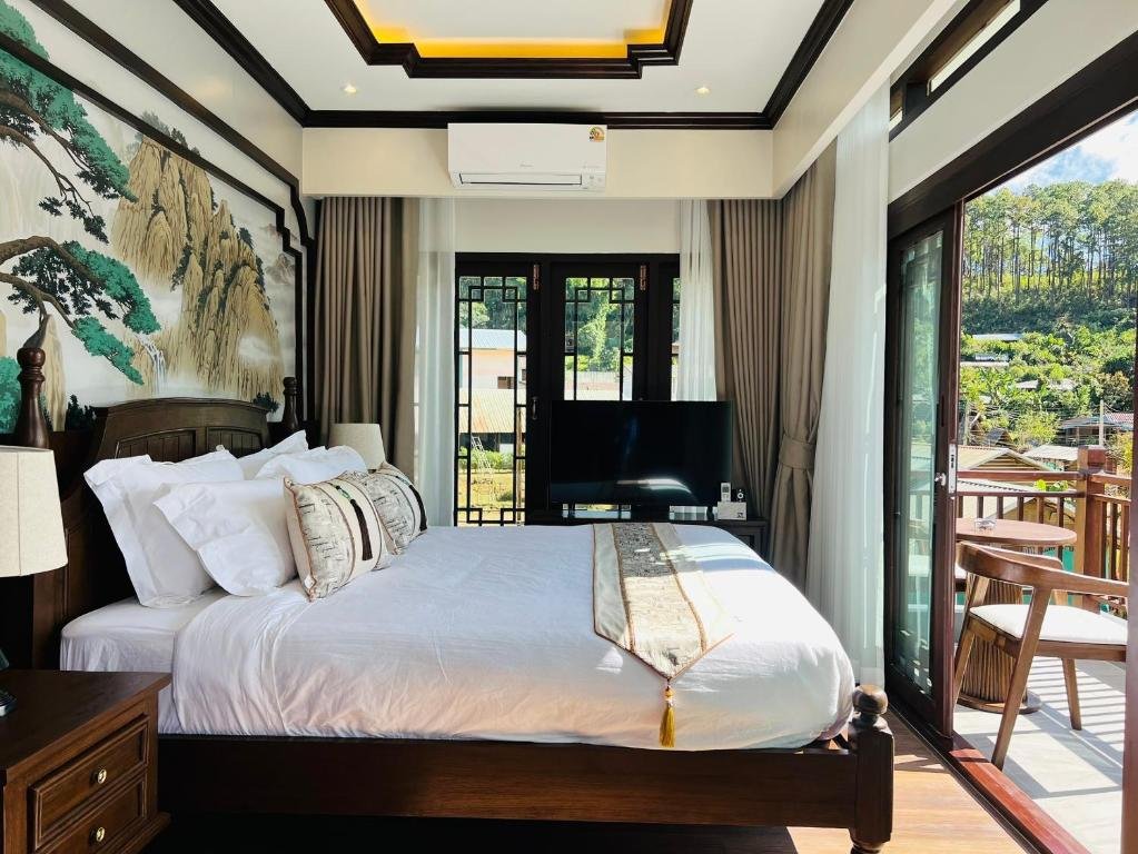ห้องนอนที่มีแสงสว่างเพียงพอพร้อมเตียงขนาดใหญ่ ประตูบานเลื่อนกระจกสู่ระเบียงที่มีเก้าอี้ ภาพจิตรกรรมฝาผนัง โทรทัศน์ และเครื่องปรับอากาศ เหมาะสำหรับการพักผ่อนหลังจากสำรวจสถานที่ท่องเที่ยวในอยุธยาและสถานที่ท่องเที่ยวอื่น ๆ ในอยุธยา แสงธรรมชาติส่องเข้ามาในห้องอย่างเต็มที่.