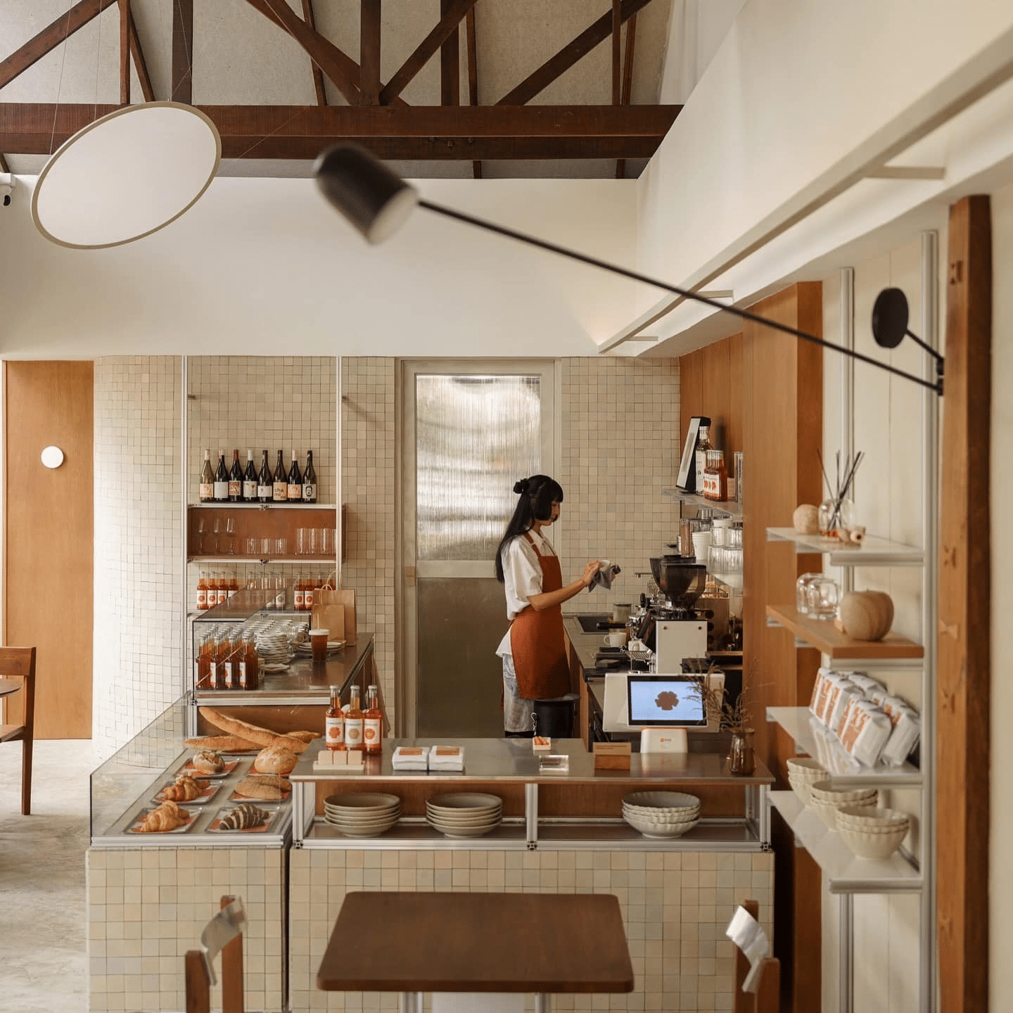 คนกำลังชงกาแฟอยู่หลังเคาน์เตอร์ในร้านเบเกอรี่คาเฟ่สมัยใหม่ในเชียงใหม่ โดยมีขนมอบจัดแสดงและชั้นวางที่เต็มไปด้วยขวดและสินค้าบรรจุภัณฑ์—จุดแวะพักที่สมบูรณ์แบบขณะเที่ยวเชียงใหม่.