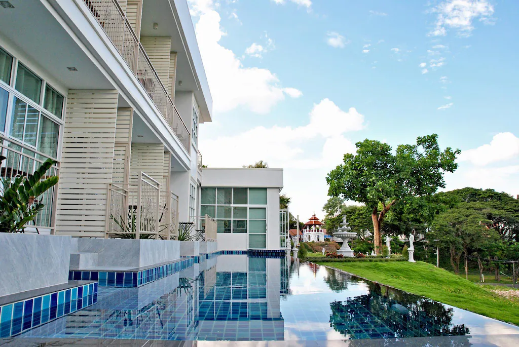 อาคารสมัยใหม่พร้อมหน้าต่างบานใหญ่และระเบียงติดสระว่ายน้ำอินฟินิตี้กลางแจ้ง ล้อมรอบด้วยสนามหญ้าเขียวขจีและต้นไม้—เหมาะสำหรับผู้ที่มองหาที่พักในปัวหรือที่พักในน่านที่มีสไตล์ภายใต้ท้องฟ้าสีครามสดใส.