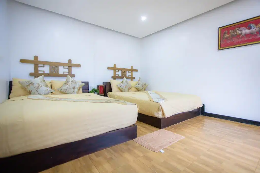 ห้องนอนที่มีเตียงใหญ่สองเตียงพร้อมผ้าปูที่นอนสีเบจ, พื้นไม้, พรมขนาดเล็ก, และภาพวาดม้าติดกรอบบนผนังสีขาว—เหมาะสำหรับการผ่อนคลายหลังจากวันที่ออกไปเที่ยวสถานที่ท่องเที่ยวในอยุธยา.